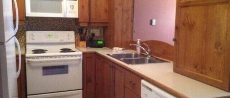 A compact kitchen with wooden cabinets, a microwave, stove, sink, and dishwasher.