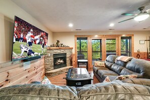 A living room with a fireplace, leather sofa, and a large TV displaying a football game.