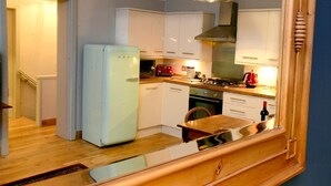 A compact kitchen with white cabinets, a white refrigerator, a stove, and a wooden dining table. - Rothay Villa (Ambleside)