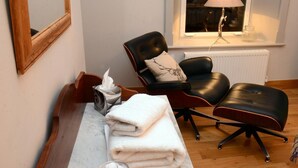 A room with a wooden bench, a black leather chair, a white radiator, and a window with a lamp. - Rothay Villa (Ambleside)