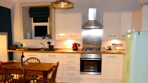 A kitchen with wooden flooring, white cabinets, a stainless steel range hood, a built-in oven, and a refrigerator. - Rothay Villa (Ambleside)
