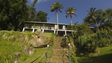 Um edifício com um caminho de pedra que leva a uma estrutura de telhado branco, cercada por vegetação exuberante e palmeiras.