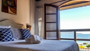 A bedroom with a large bed, two patterned pillows, a rolled towel, and a view of the sea through an open window. - Pousada Três Coqueiros (Angra dos Reis)