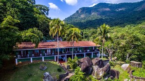 A two-story building with a red-tiled roof, surrounded by lush greenery and large rocks. - Pousada Três Coqueiros (Angra dos Reis)