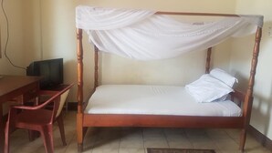 Una cama individual con dosel, un escritorio de madera y una silla en una habitación con suelo de baldosas.