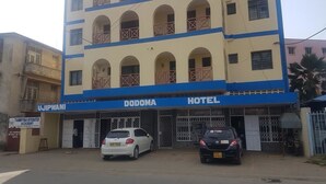 Un edificio con un letrero que indica 'Dodoma Hotel' y 'Tahmiyyan Integrated Academy' debajo. Hay dos coches estacionados en la parte delantera.