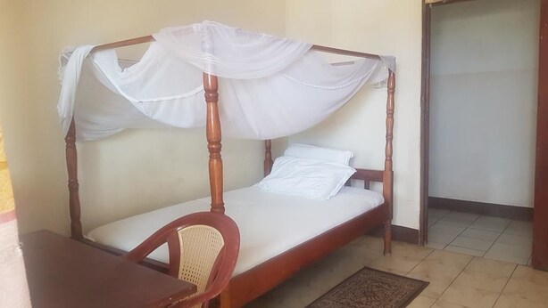 Una cama individual con estructura de madera y dosel, una silla de madera y una mesita pequeña.