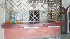 Una recepción con mostrador de ladrillo rojo, una puerta de seguridad metálica y una pequeña exhibición de flores.