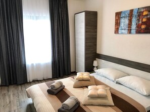 A hotel room with a bed, pillows, a bedside table with a lamp, a large painting on the wall, and a window with curtains. - Guest House Klanfar (Rakovica)