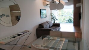 A modern living room with a glass coffee table, a brown sofa, a large mirror, and a framed picture on the wall. - Rio de Janeiro Season. Bora Bora Barra - Complete Leisure Resort - Barra da Tijuca - RJ (Rio de Janeiro)