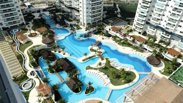 A resort with multiple swimming pools, palm trees, and a central water feature. - Rio de Janeiro Season. Bora Bora Barra - Complete Leisure Resort - Barra da Tijuca - RJ (Rio de Janeiro)
