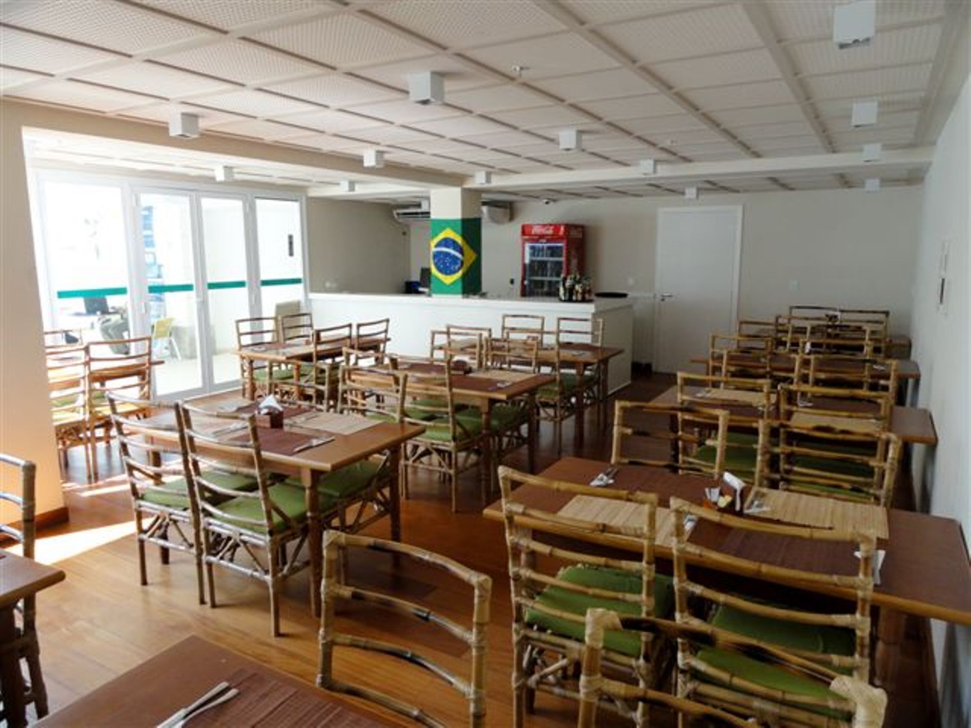 Un espace repas avec des tables et des chaises en bois, un drapeau brésilien et un réfrigérateur en arrière-plan.