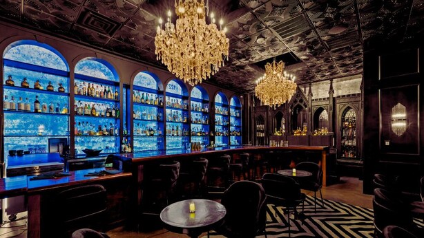 A bar area with shelves of bottles, chandeliers, and seating. - Inn Cahoots on 6th: 10BR/26Bed - Pool,Roofdeck, Garden Bars, Walk To Everything! (Austin)