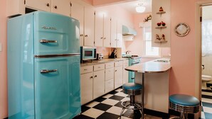 Eine Küche im Retro-Stil mit einem türkisblauen Kühlschrank, weißen Schränken, einer Mikrowelle und einem Schachbrettboden.