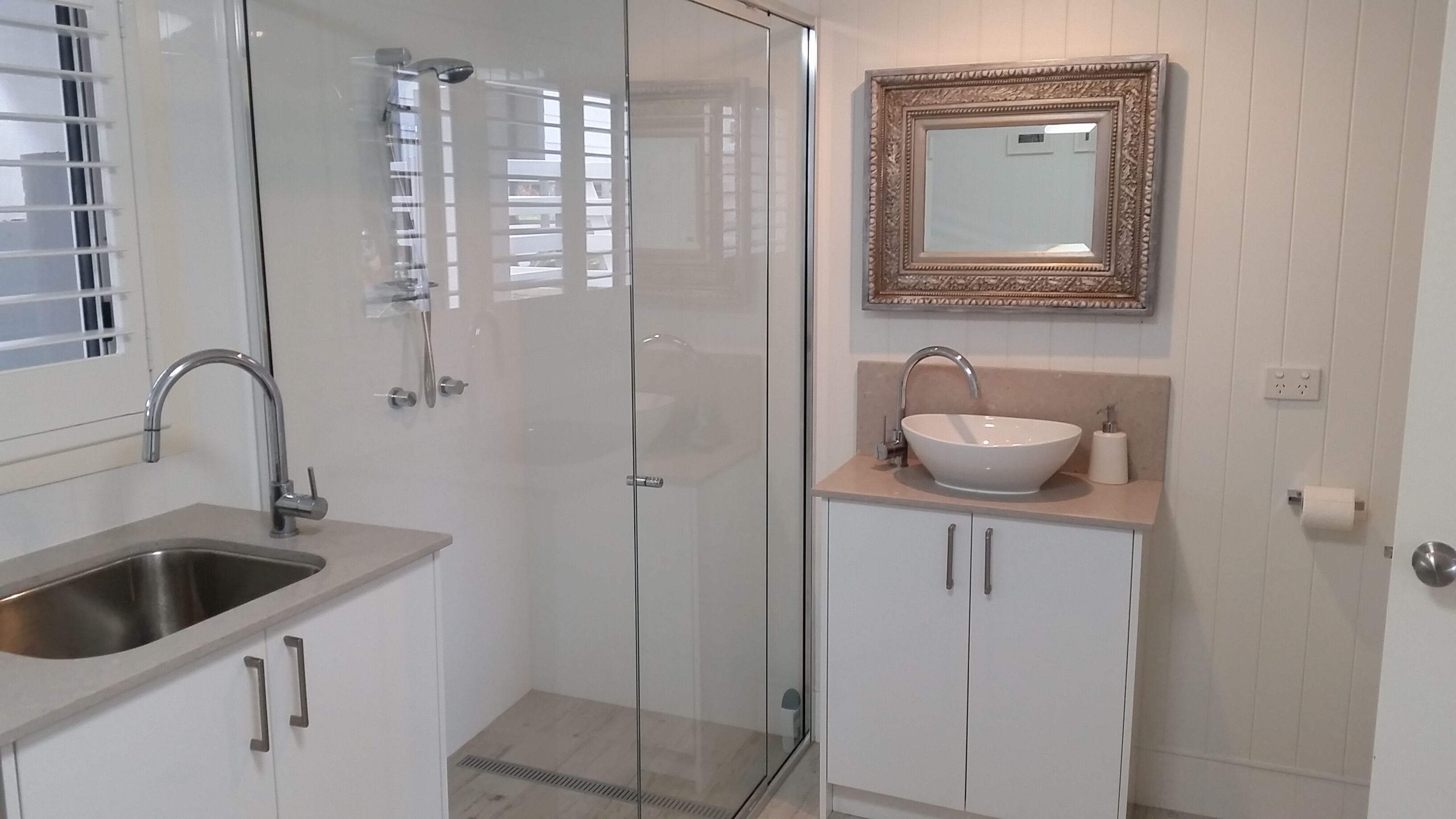 A modern bathroom with a glass shower enclosure, a sink with a mirror above, and a toilet with a roll of toilet paper.