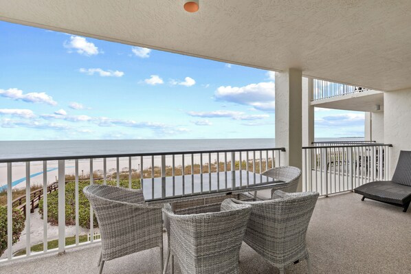 Ein Balkon mit Korbmöbeln, einem Glastisch und Blick auf Strand und Meer.