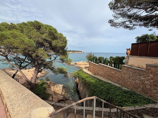 A coastal landscape with a stone staircase, a pine tree, and a view of the sea. - Beautiful apartment with large terrace and spectacular views of Sant Pol bay (S'Agaró)