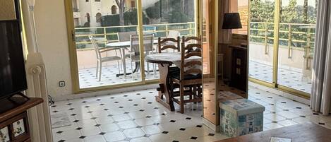 Una sala de estar con piso de baldosas, un sofá, una mesa y un balcón con vistas al exterior.