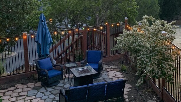 Une terrasse extérieure avec un sol en pierre, des meubles de jardin bleus et une clôture décorative agrémentée de guirlandes lumineuses.