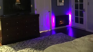 Une pièce avec une commode en bois foncé, un téléviseur posé dessus, une porte avec une lumière violette et une cheminée.