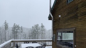 Puinen mökki, jossa on parveke, ja parvekkeella on pöytä ja tuolit. Mökkiä ympäröivät lumipeitteiset puut.
