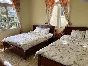 Two single beds with matching headboards and footboards, a nightstand, and large windows with a view of the surrounding greenery.