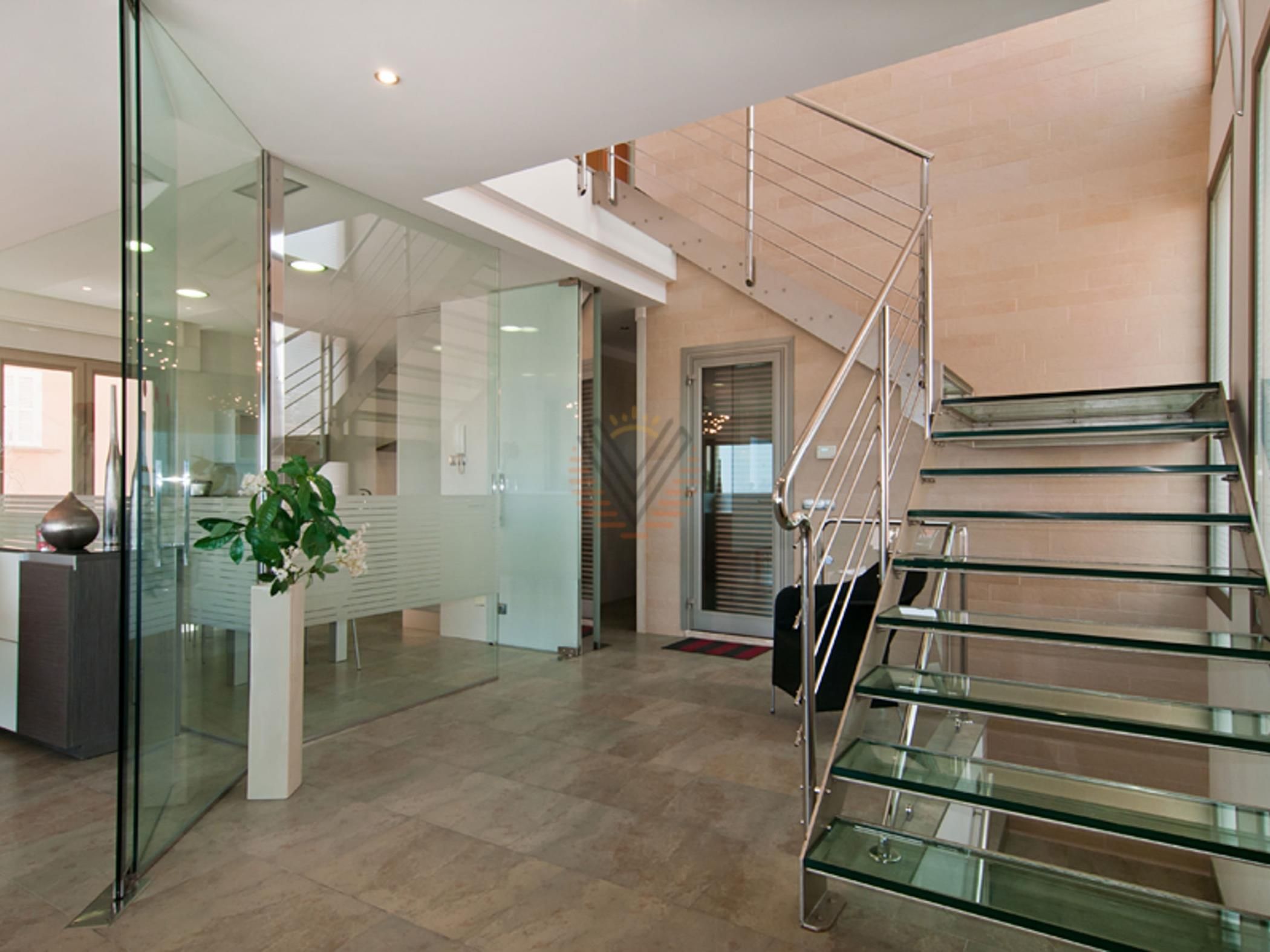 A modern interior with a glass staircase, a reception desk, and a potted plant.