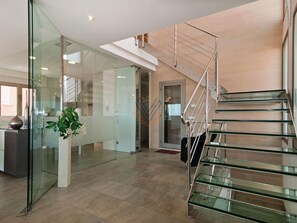 Un interior modern amb una escala de vidre, una recepció i una planta en test.