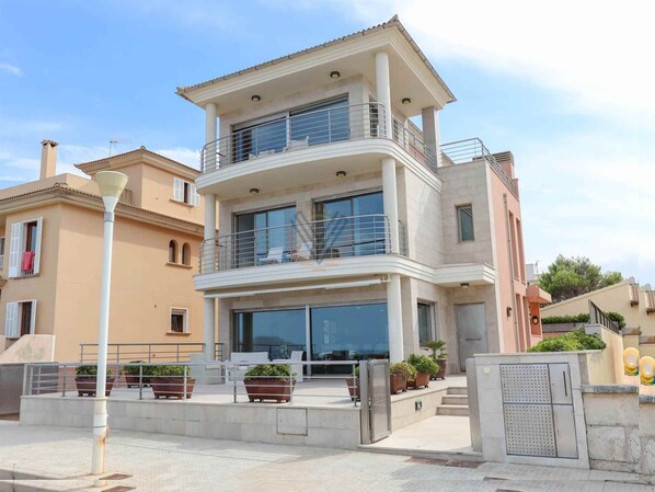 A multi-story residential building with balconies, large windows, and a paved entrance area with potted plants. - Bohemi, luxury seafront villa (Santa Margalida - Can Picafort/Son Serra Marina)