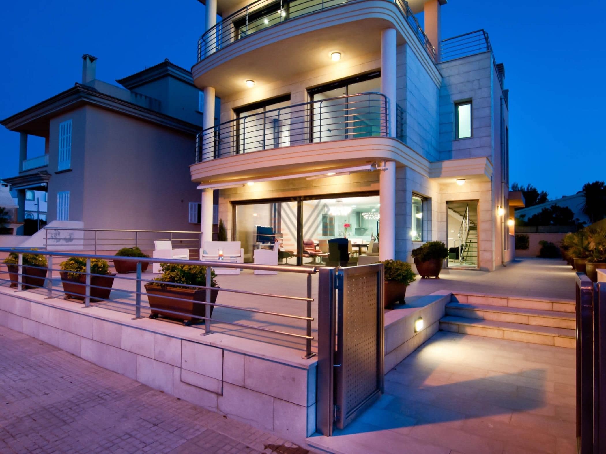 Un bâtiment moderne à deux étages, doté d’un balcon, d’un espace extérieur aménagé pour s’asseoir et d’une entrée sécurisée par un portail.