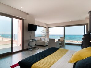 Un dormitori modern amb un llit gran, un televisor de pantalla plana, un sofà i un balcó amb vista al mar.