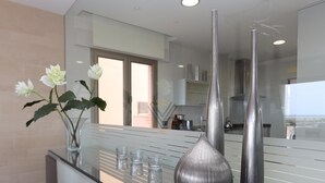 Ett modernt kök med en bänkskiva i glas, två metallvaser och en vas med vita blommor.