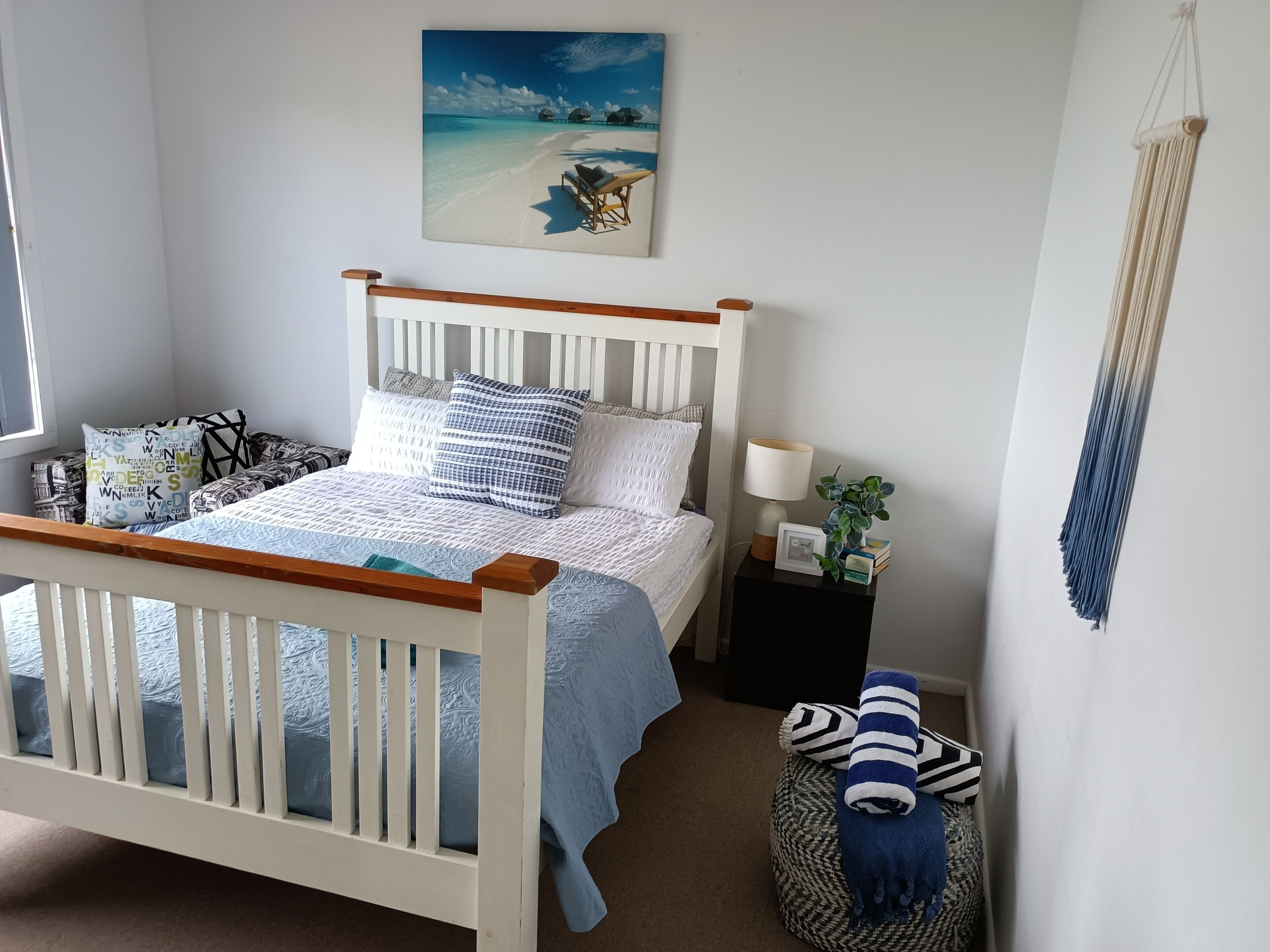 A bedroom with a bed, bedside table, lamp, and a wall hanging.