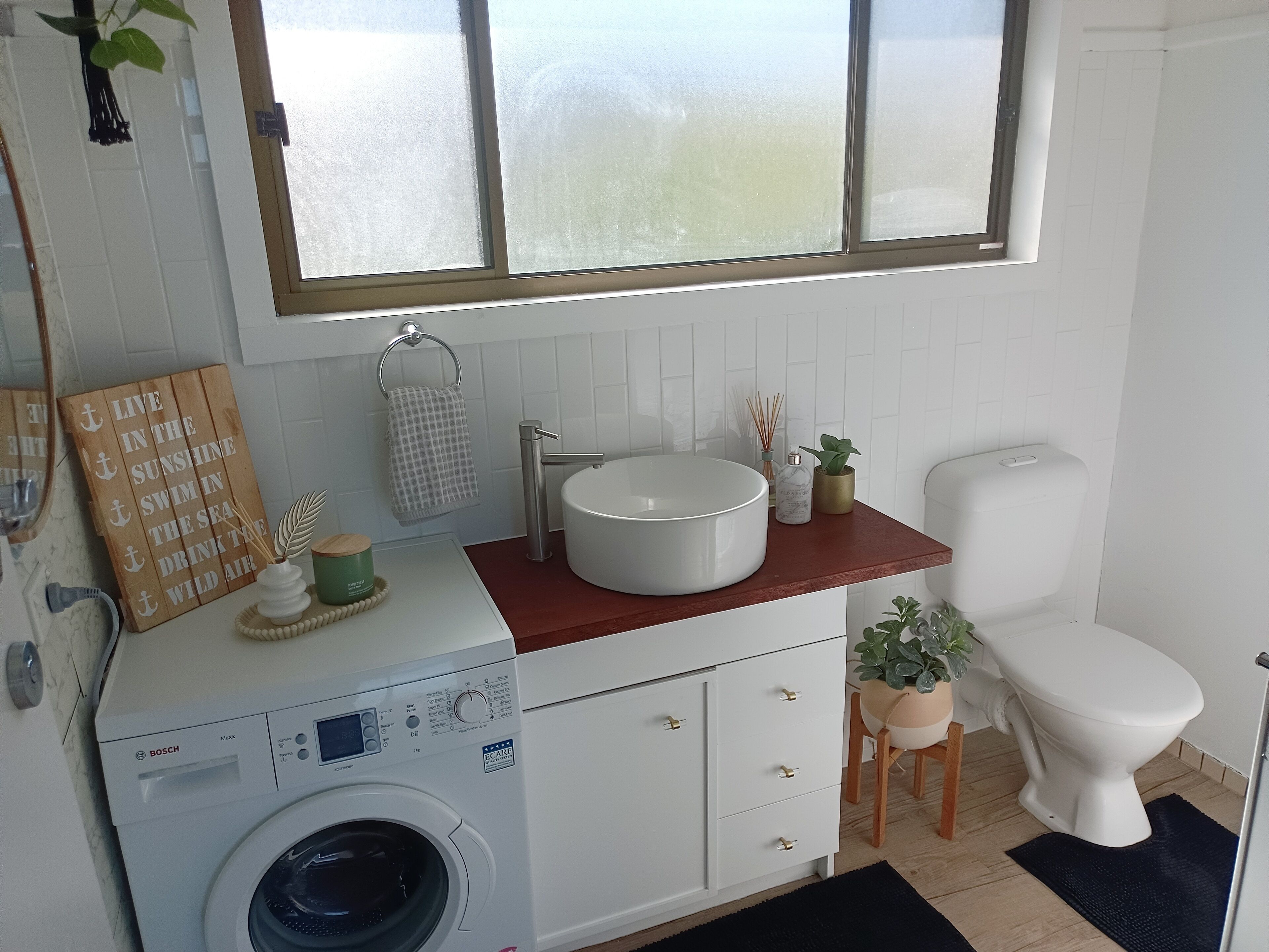 A modern bathroom with a Bosch washing machine, a sink, a toilet, and a window with a view of the outdoors.