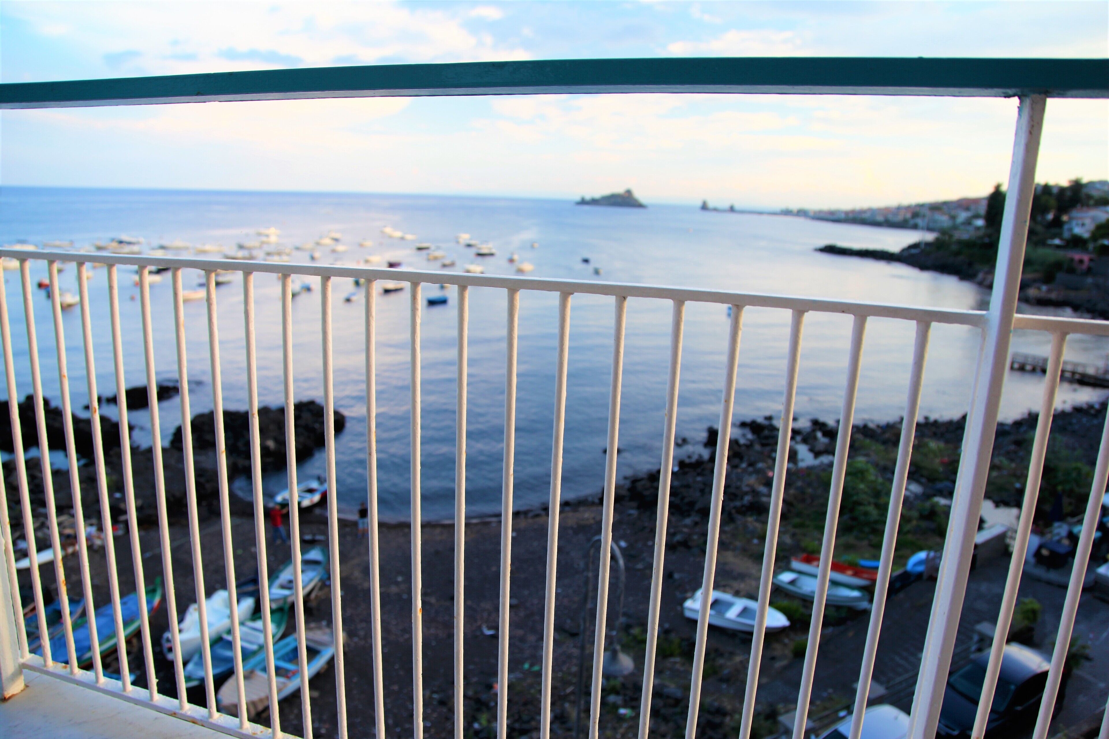 A balcony with a view of the sea, boats, and a rocky shoreline.