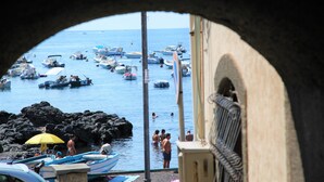 A view through a doorway of a harbor with boats, people, and a rocky shoreline.
