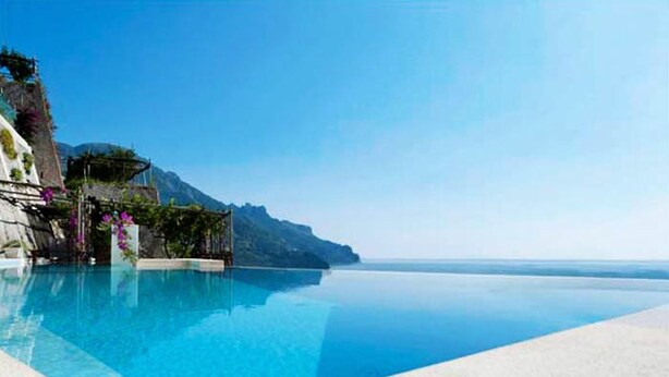 A clear blue pool with a view of a mountain and the sea.
