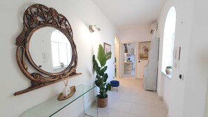 A hallway with a large ornate mirror, a glass console table, and potted plants.
