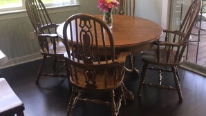 Un comedor con una mesa redonda de madera rodeada por cuatro sillas, un jarrón con flores y un cuadro en la pared.