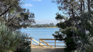 A gravel path leading to a wooden bench overlooking a body of water, surrounded by trees and a clear sky. - Spacious and unique beach cottage for relaxing getaways (Barwon Heads)