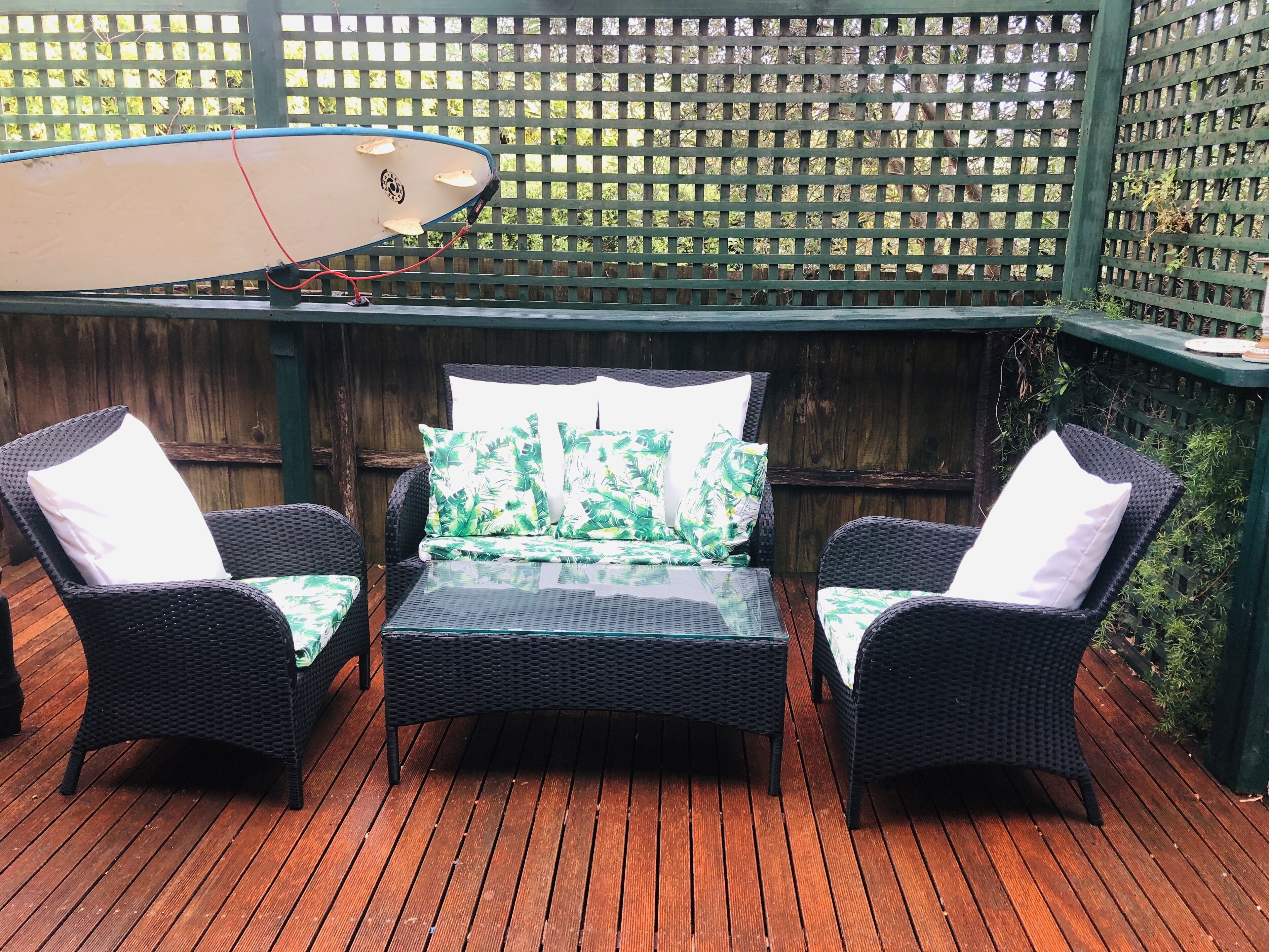 A patio with wicker furniture, a glass table, and a surfboard.