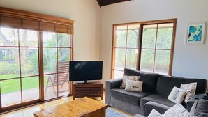 A spacious living room with a large sofa set, a wooden coffee table, and a television on a stand. - Spacious and unique beach cottage for relaxing getaways (Barwon Heads)
