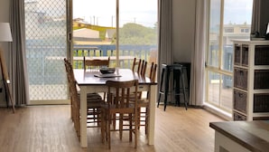 A spacious room with a large dining table, wooden chairs, and a view of the outdoors through large windows. - Sable Blanc on Newell - dogs allowed - 3 min walk to the beach & fabulous views. (Middleton)