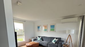 A modern living room with a grey sofa, a blue armchair, and a wooden floor. - Sable Blanc on Newell - dogs allowed - 3 min walk to the beach & fabulous views. (Middleton)