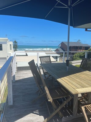 Una terraza de madera con mesa y sillas, con vista a la playa.