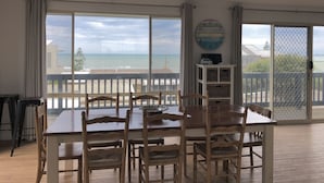 A dining area with a large table and chairs, a clock on the wall, and a view of the beach through large windows. - Sable Blanc on Newell - dogs allowed - 3 min walk to the beach & fabulous views. (Middleton)