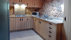 A kitchen with wooden cabinets, a granite countertop, a microwave, and a stone wall. - Stone Cottage The Compostelana (Curtis)
