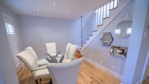 A dining area with a glass table and white chairs, a staircase with wooden steps, and a hexagonal mirror on the wall. - Shoal Creek Greenbelt (Austin)