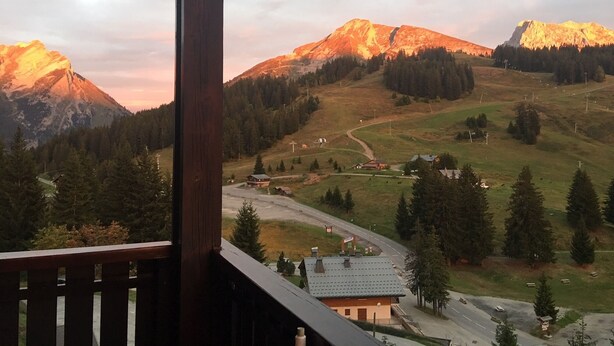 A mountain landscape with a wooden balcony overlooking a road and buildings. - La Tournette apartment Les Maisons des Bois (Manigod)