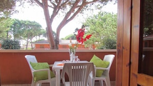 Een terras met een tafel en stoelen, een vaas met bloemen, en een grote boom op de achtergrond.